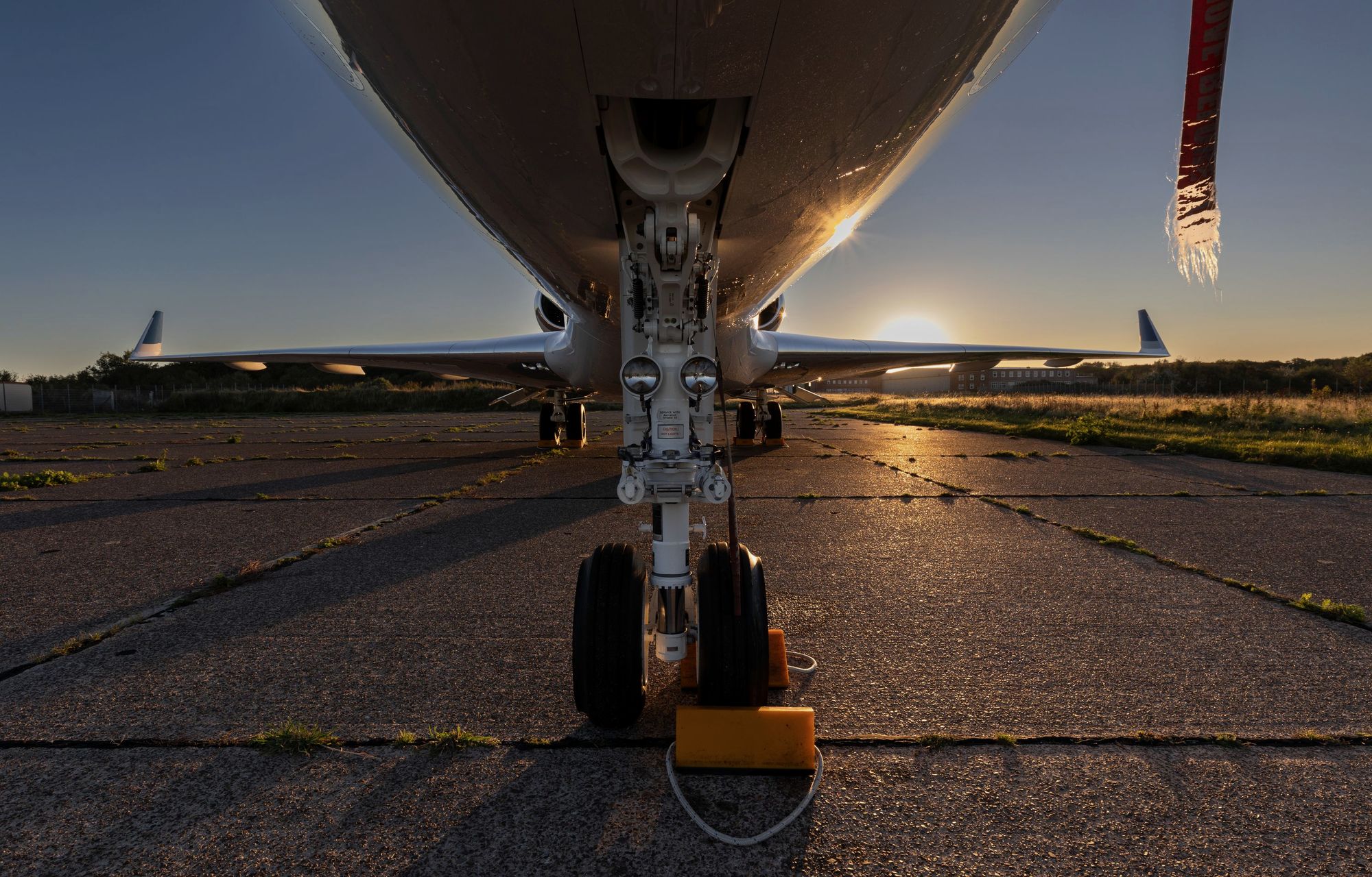 Low view of a business jet's nose gear, chocked on the ramp as the sun sets